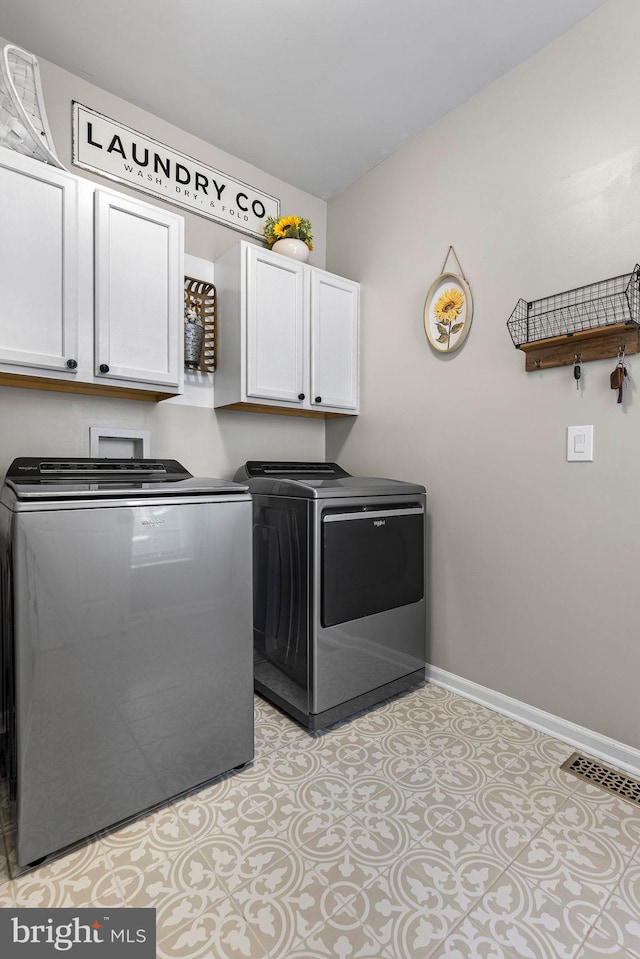 clothes washing area featuring washer and clothes dryer, light tile patterned flooring, and cabinets