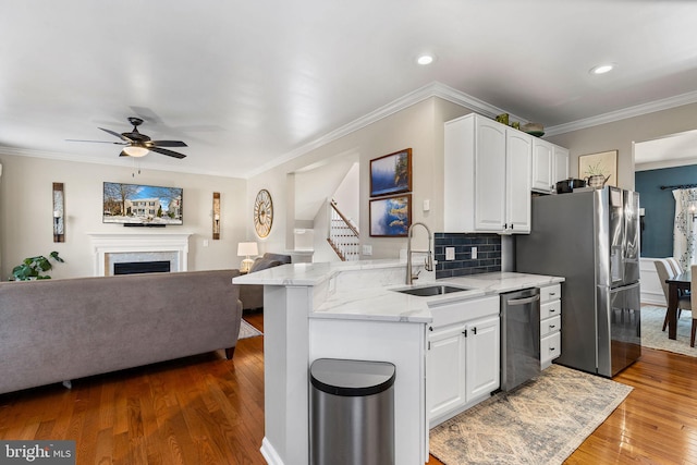 kitchen with kitchen peninsula, appliances with stainless steel finishes, light stone countertops, sink, and white cabinetry