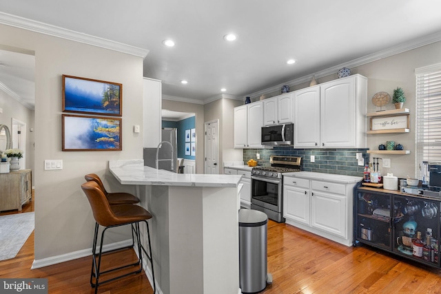 kitchen featuring stainless steel appliances, light hardwood / wood-style flooring, kitchen peninsula, a breakfast bar, and white cabinets