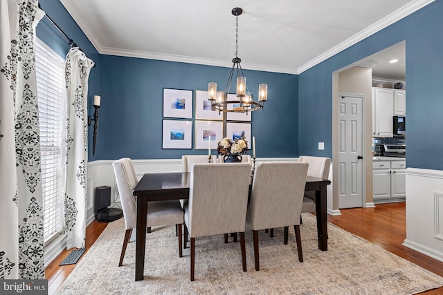 dining space with hardwood / wood-style flooring, ornamental molding, and a chandelier