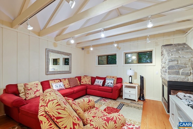 living room with lofted ceiling with beams, a stone fireplace, rail lighting, and light hardwood / wood-style flooring