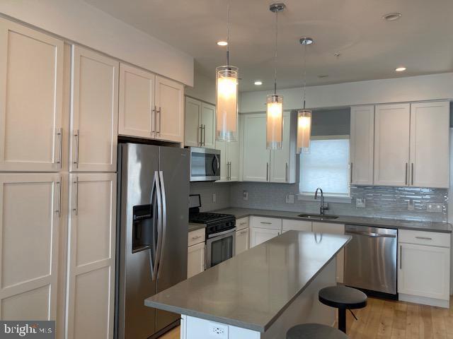 kitchen with sink, stainless steel appliances, a kitchen island, and white cabinetry