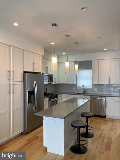 kitchen with stainless steel appliances, a center island, hanging light fixtures, white cabinets, and sink