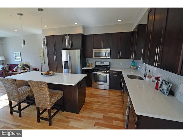 kitchen featuring a center island, decorative light fixtures, stainless steel appliances, sink, and a kitchen breakfast bar