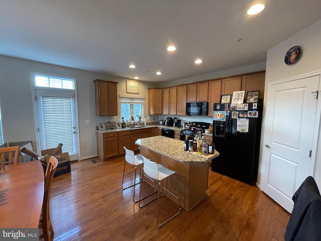 kitchen featuring light stone countertops, a kitchen bar, a kitchen island, black appliances, and hardwood / wood-style flooring