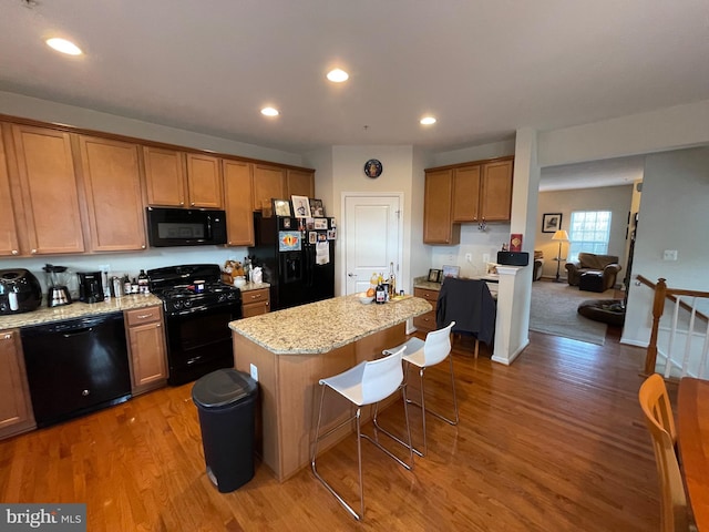 kitchen featuring light stone countertops, light wood-type flooring, a breakfast bar, black appliances, and a kitchen island