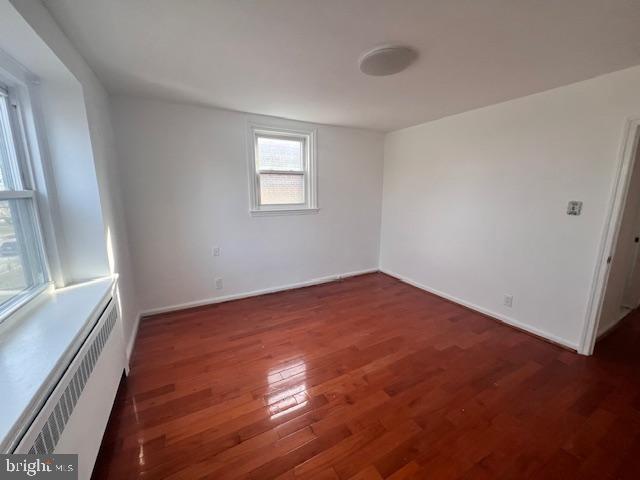 empty room featuring dark hardwood / wood-style flooring and radiator heating unit