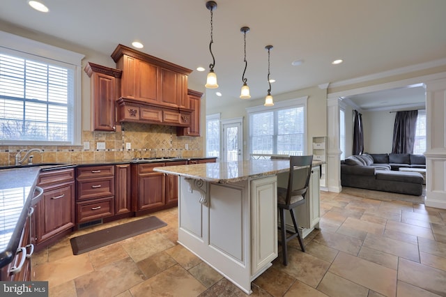 kitchen with tasteful backsplash, a kitchen island, a kitchen bar, hanging light fixtures, and light stone countertops