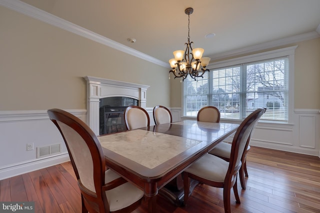 dining space with dark wood-type flooring, ornamental molding, and a notable chandelier