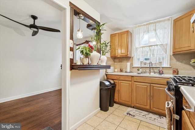 kitchen featuring light tile patterned floors, ceiling fan, stainless steel gas range oven, sink, and decorative light fixtures