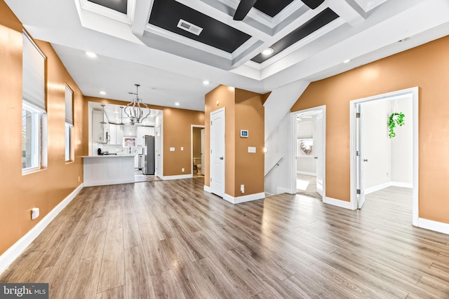 unfurnished living room featuring ornamental molding, coffered ceiling, beam ceiling, an inviting chandelier, and light hardwood / wood-style floors