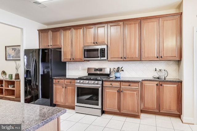 kitchen featuring decorative backsplash, stainless steel appliances, dark stone countertops, and light tile patterned flooring