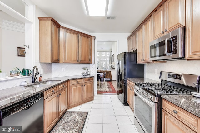 kitchen featuring sink, dark stone countertops, light tile patterned floors, appliances with stainless steel finishes, and tasteful backsplash