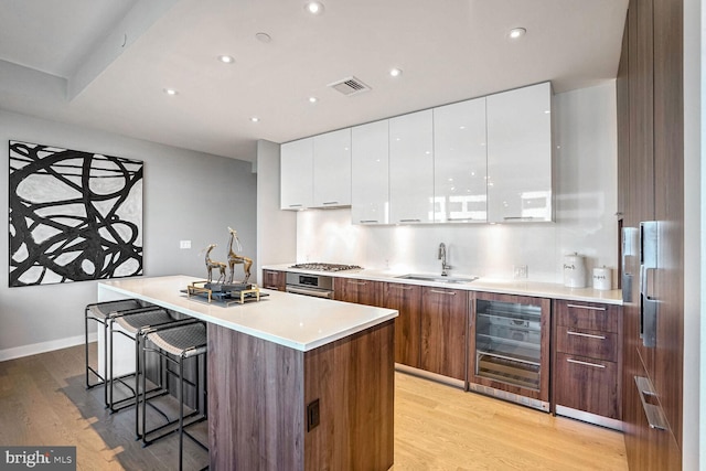 kitchen with white cabinets, light wood-type flooring, sink, and wine cooler