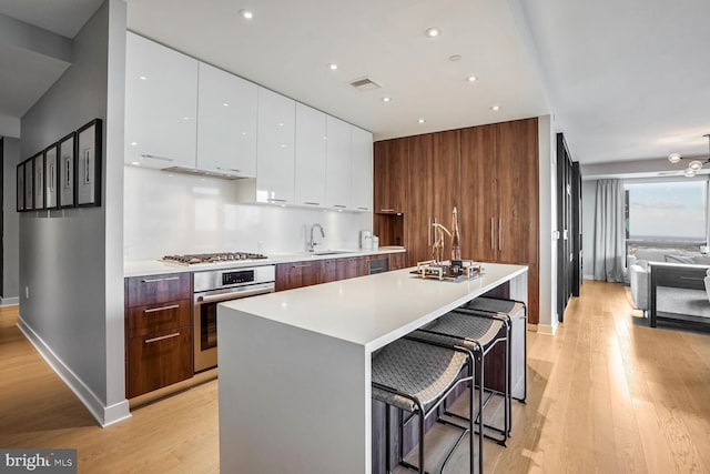 kitchen featuring sink, stainless steel appliances, an island with sink, a kitchen bar, and white cabinets