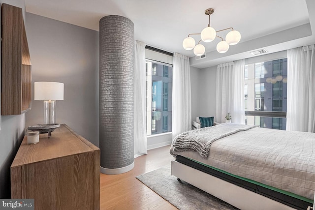 bedroom with a notable chandelier, light wood-type flooring, and multiple windows