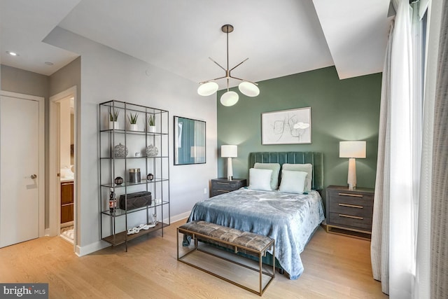 bedroom featuring ensuite bathroom, an inviting chandelier, and light hardwood / wood-style flooring