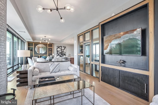 living room featuring a raised ceiling, light hardwood / wood-style floors, an inviting chandelier, and built in shelves