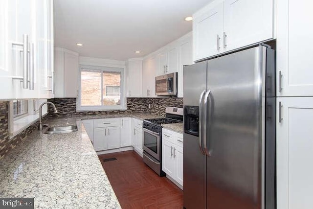 kitchen featuring light stone countertops, appliances with stainless steel finishes, backsplash, sink, and white cabinetry