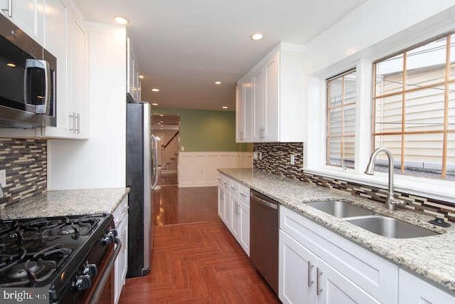 kitchen with white cabinetry, sink, light stone counters, dark parquet floors, and appliances with stainless steel finishes