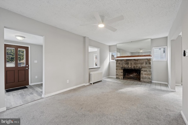 unfurnished living room featuring a stone fireplace, radiator heating unit, light colored carpet, and a textured ceiling