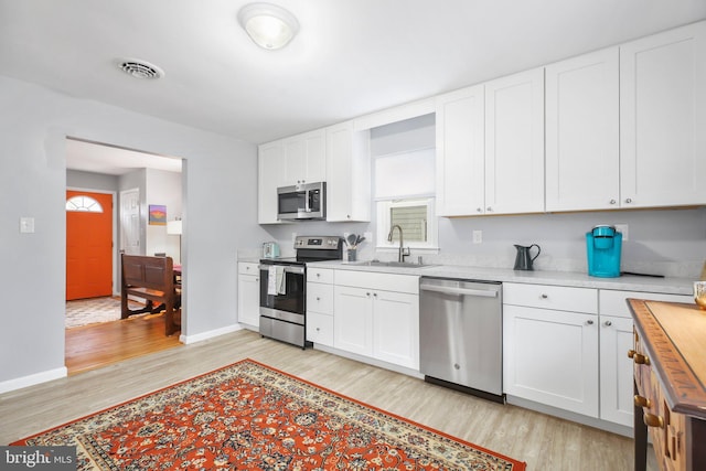 kitchen featuring white cabinets, appliances with stainless steel finishes, light hardwood / wood-style floors, and sink