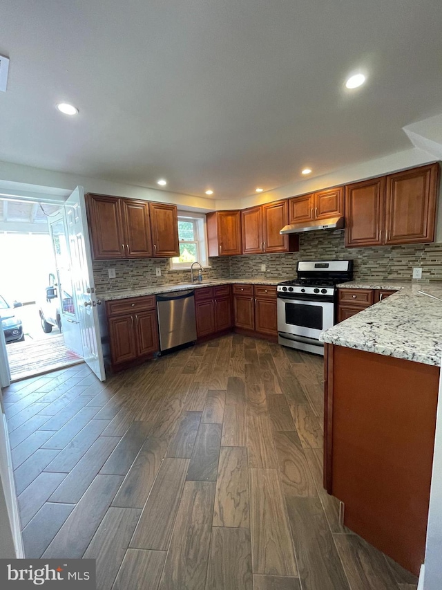 kitchen featuring sink, stainless steel appliances, light stone counters, dark hardwood / wood-style flooring, and range hood