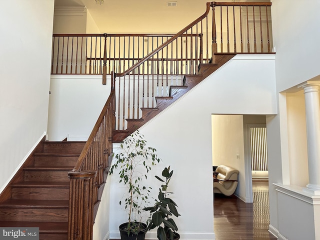 stairway featuring hardwood / wood-style floors, a high ceiling, and decorative columns