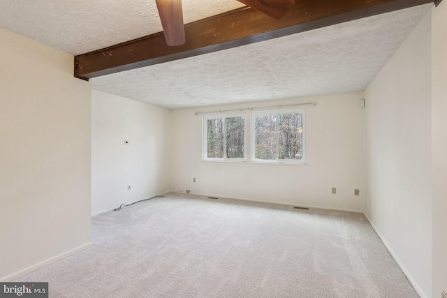 spare room featuring light carpet, beam ceiling, and a textured ceiling