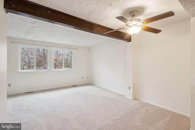 carpeted empty room with ceiling fan, beamed ceiling, and a textured ceiling