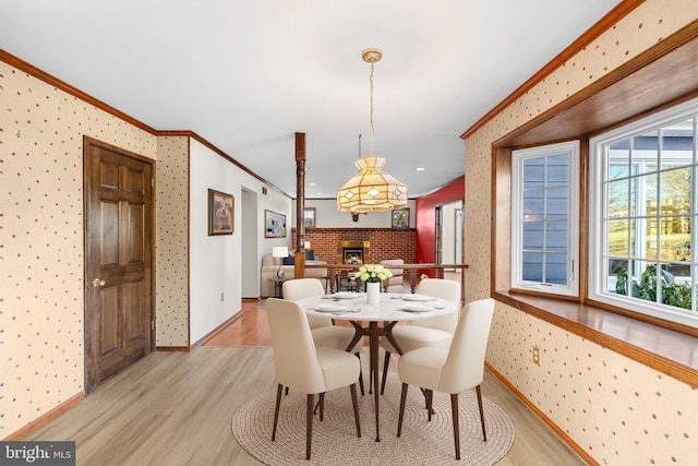 dining space with ornamental molding, a brick fireplace, and light hardwood / wood-style floors