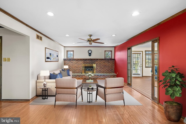 living room with crown molding, a brick fireplace, ceiling fan, and light hardwood / wood-style floors