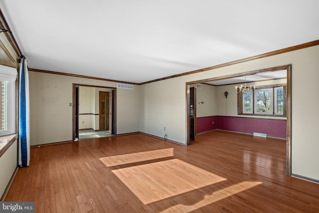 empty room with hardwood / wood-style flooring, crown molding, and an inviting chandelier