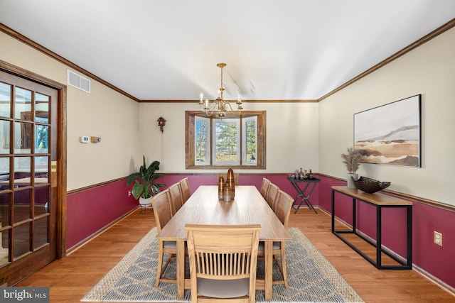 dining area featuring crown molding, a chandelier, and light hardwood / wood-style floors