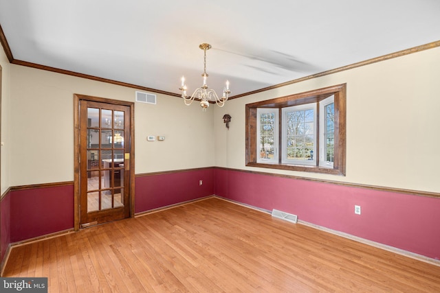 spare room featuring an inviting chandelier, wood-type flooring, and ornamental molding