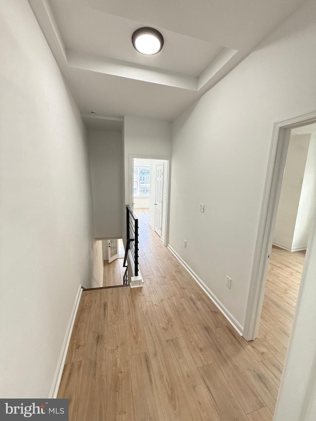 hall with light hardwood / wood-style floors and a raised ceiling