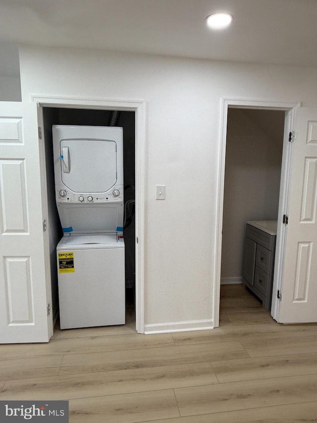 laundry room with stacked washer / drying machine and light wood-type flooring