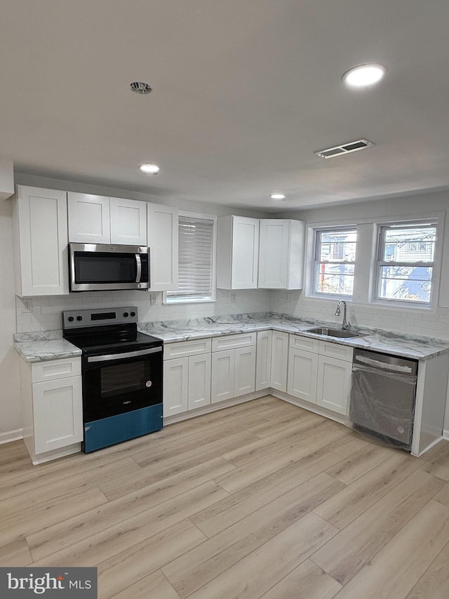 kitchen with white cabinets, sink, appliances with stainless steel finishes, and light hardwood / wood-style flooring