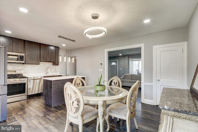 kitchen with dark wood-type flooring, dark brown cabinetry, decorative light fixtures, a center island, and stainless steel appliances