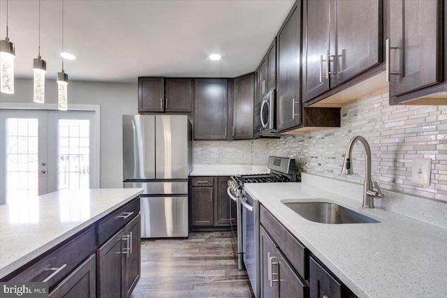 kitchen featuring dark brown cabinetry, sink, light stone counters, decorative light fixtures, and appliances with stainless steel finishes