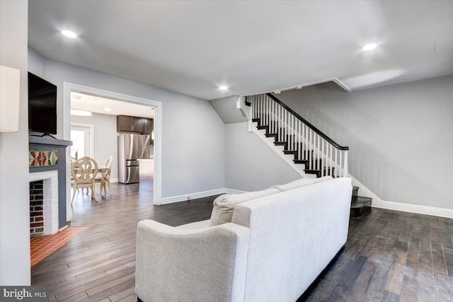 living room with a brick fireplace and dark hardwood / wood-style flooring