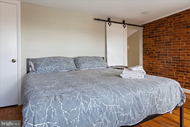 bedroom featuring wood-type flooring, a barn door, and brick wall