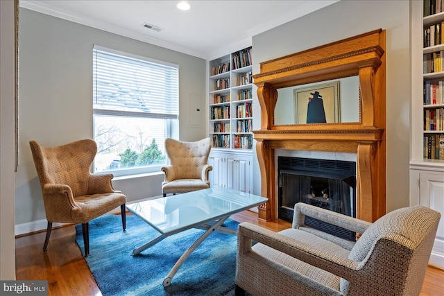 living area with built in shelves, ornamental molding, and hardwood / wood-style flooring