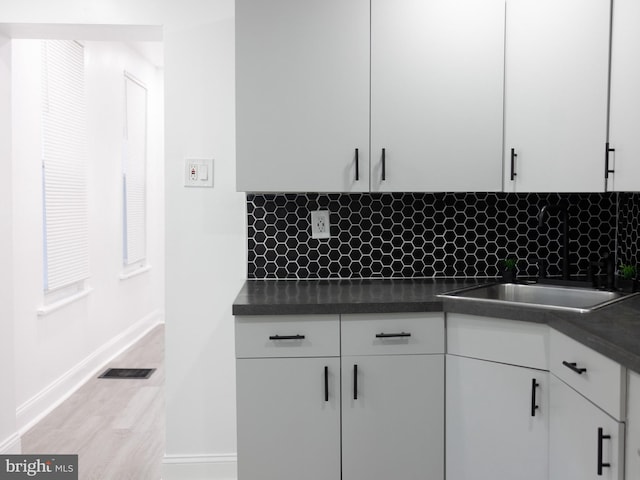 kitchen featuring decorative backsplash, light hardwood / wood-style floors, white cabinetry, and sink