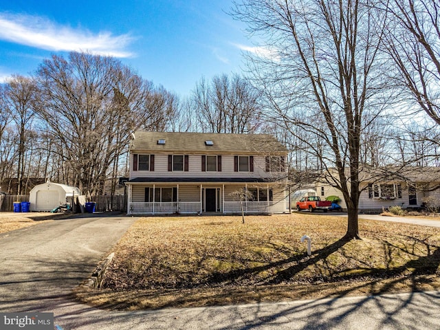 view of front facade featuring covered porch, a storage shed, aphalt driveway, and an outdoor structure