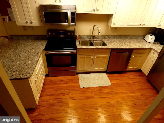 kitchen featuring dishwasher, sink, light wood-type flooring, light stone countertops, and electric range oven