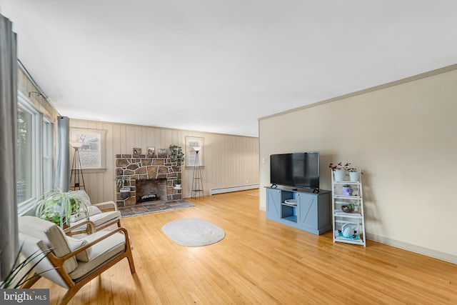 living room featuring baseboard heating, a stone fireplace, ornamental molding, and hardwood / wood-style floors