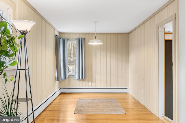 unfurnished room with a baseboard heating unit, wood walls, and light hardwood / wood-style flooring