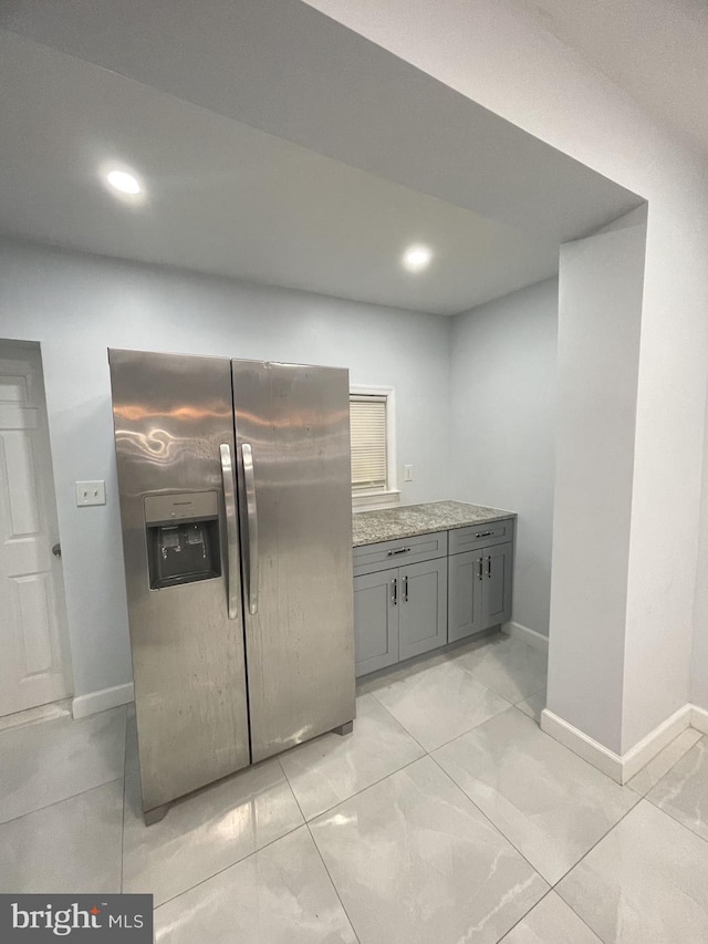 kitchen with gray cabinets, stainless steel fridge with ice dispenser, and light stone countertops