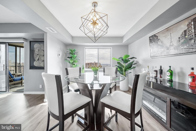 dining area featuring a tray ceiling, visible vents, light wood-style flooring, an inviting chandelier, and baseboards